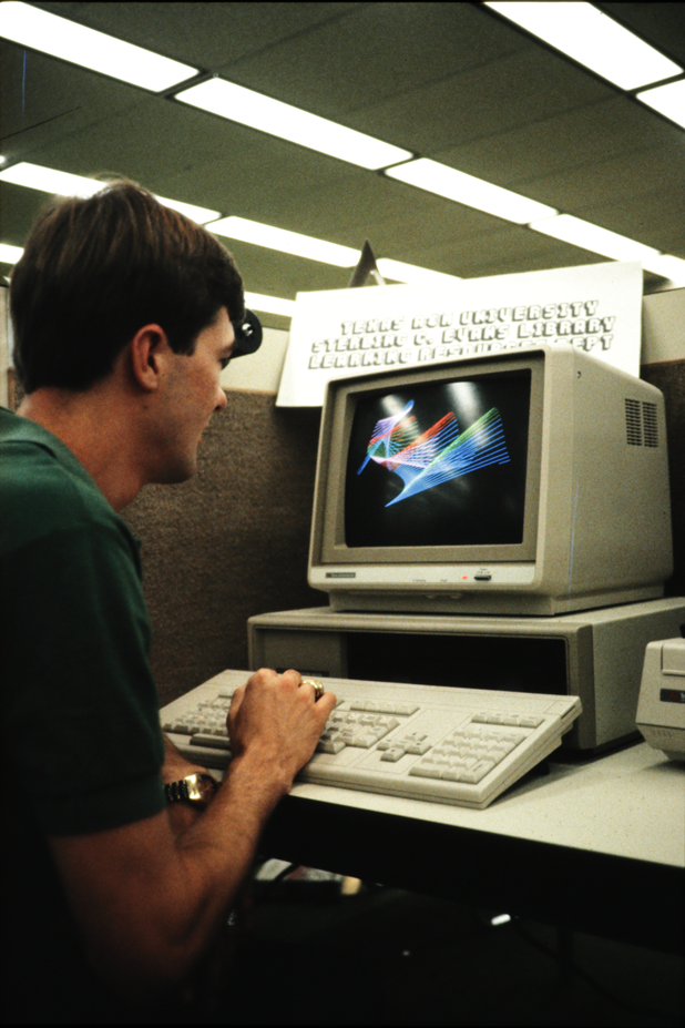 Person using a desktop computer at a library workstation, with a CRT monitor showing colorful line graphics.