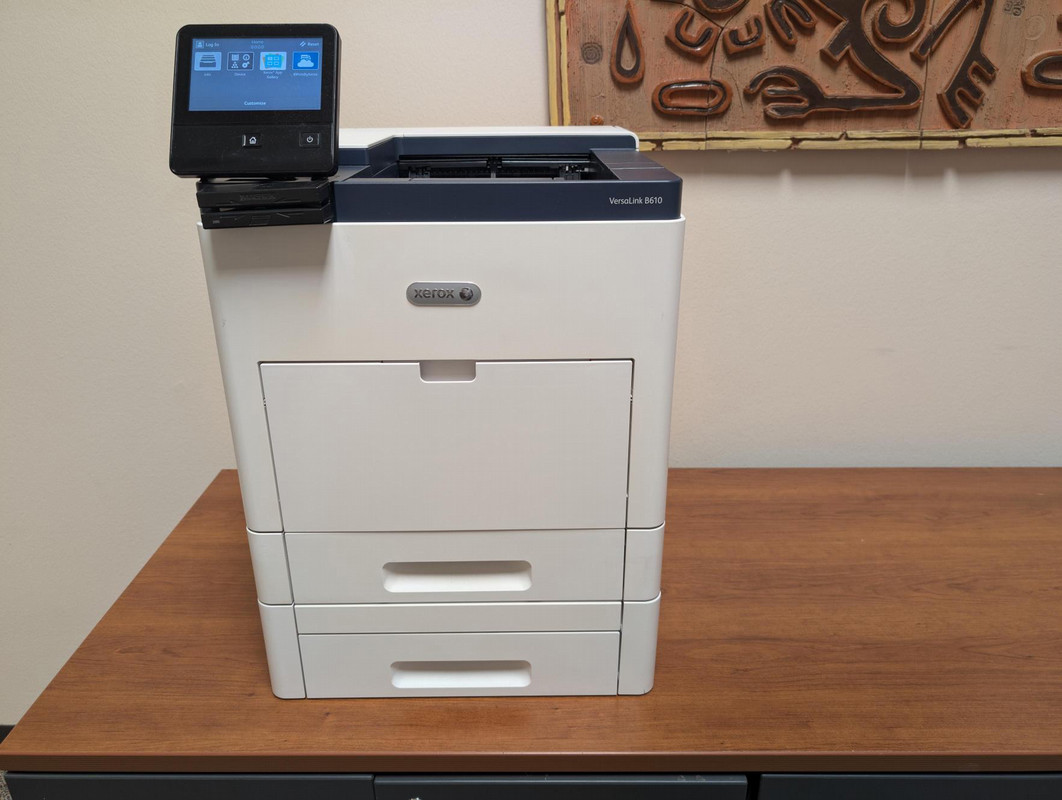 A color multifunction printer placed on a wooden cabinet alongside a touchscreen control panel.