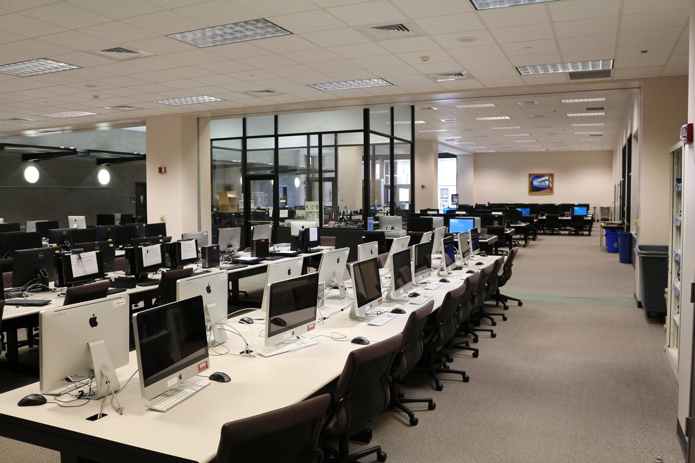 A modern computer lab featuring rows of Apple iMacs on workstations, with a spacious layout and bright lighting.